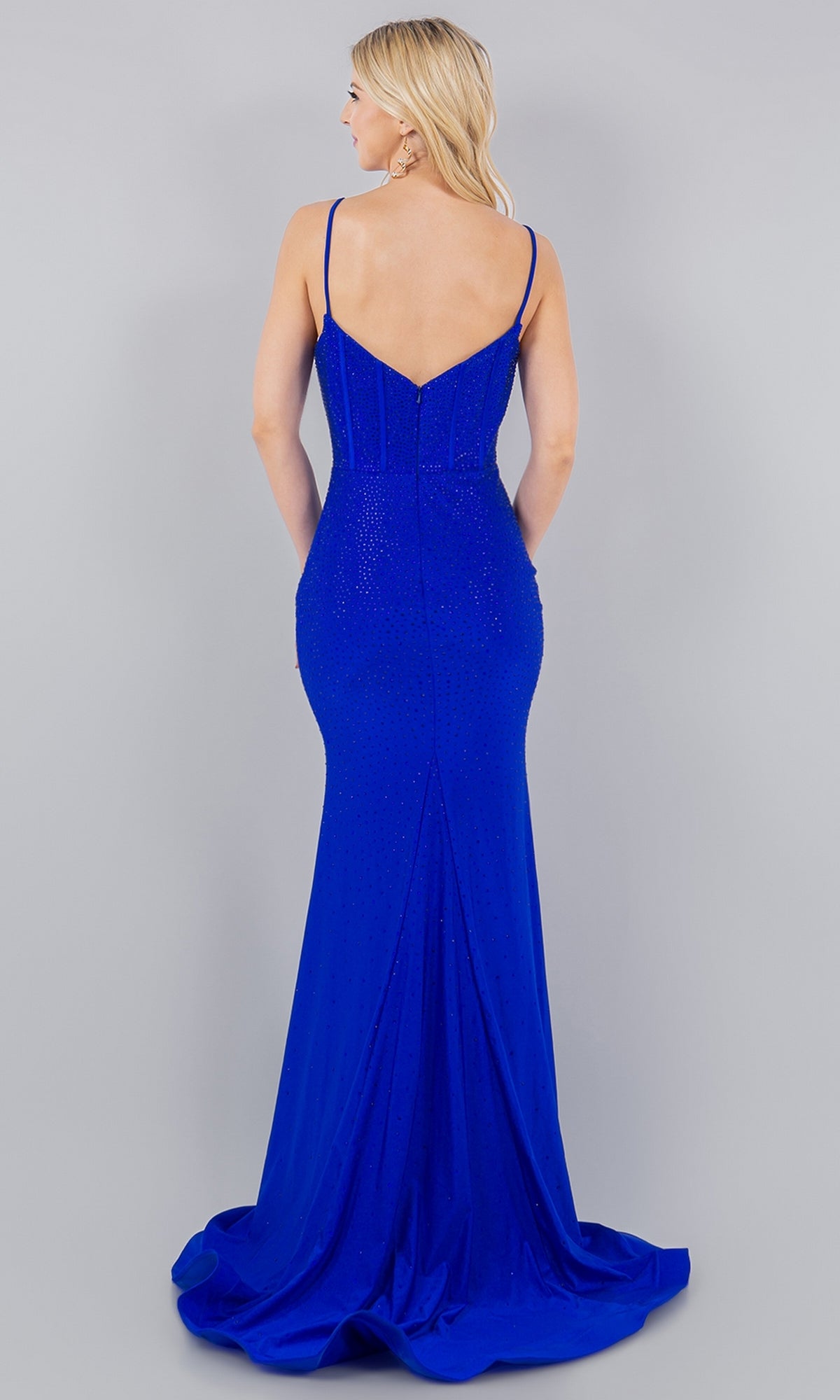 A woman faces away, wearing the Cinderella Couture 8084J Corset Beaded Prom Dress—a floor-length, royal blue gown with thin straps and a deep V-back.